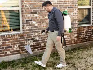 Preferred Pest Management technician applying general pest control treatment along the foundation of a Richardson, TX home