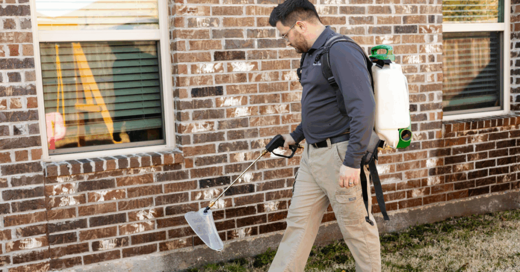 Licensed pest control technician from Preferred Pest Management treating the exterior of a Plano TX home