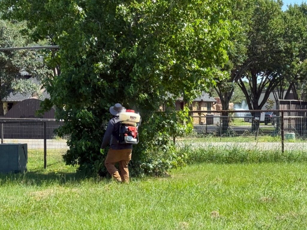 Preferred Pest Management technician applying mosquito control treatment in a shaded yard in Wylie, TX