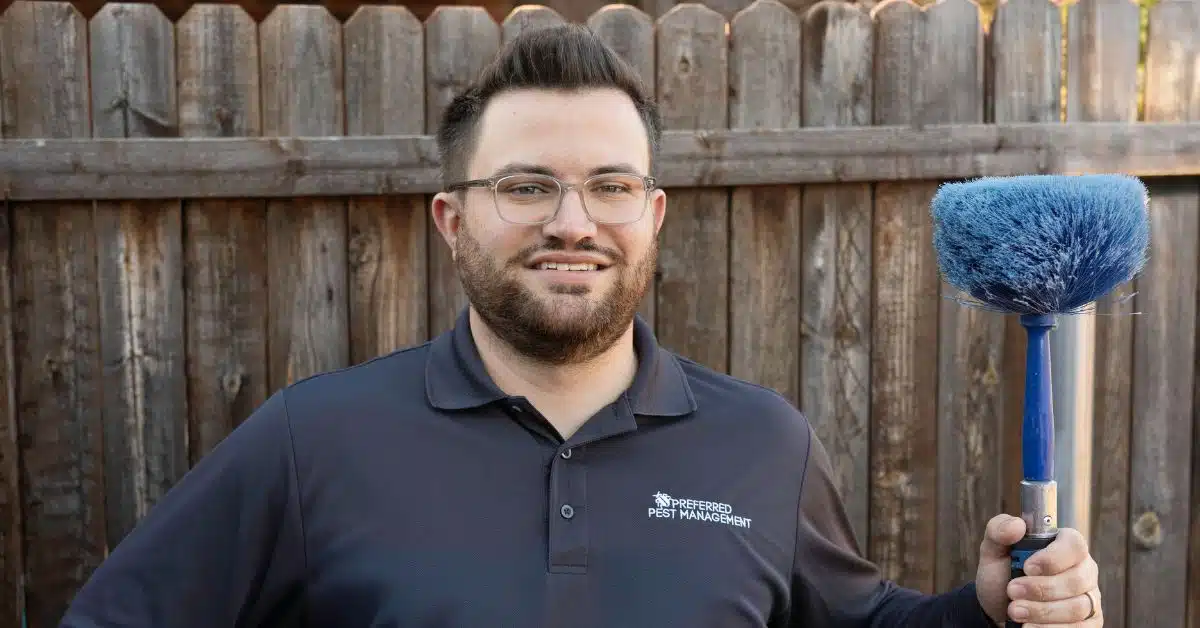 Preferred Pest Management technician holding a web removal brush after spider control service in Royse City, TX.