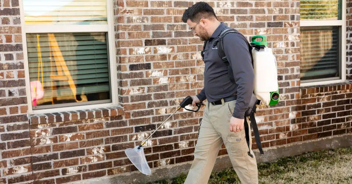 Preferred Pest Management technician performing ant control treatment along a Rowlett TX home exterior brick wall